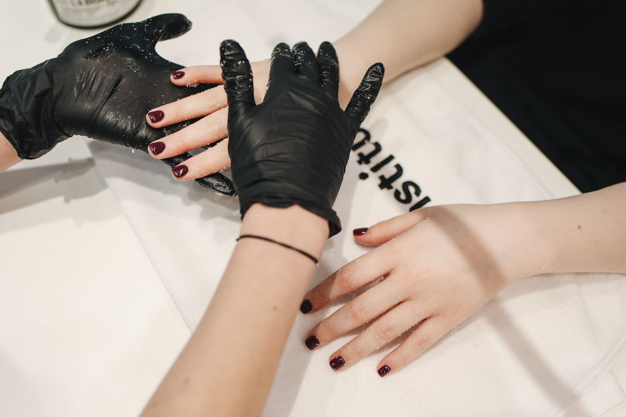 Close-up of a manicure session with black gloves applying hand treatment in a salon setting.